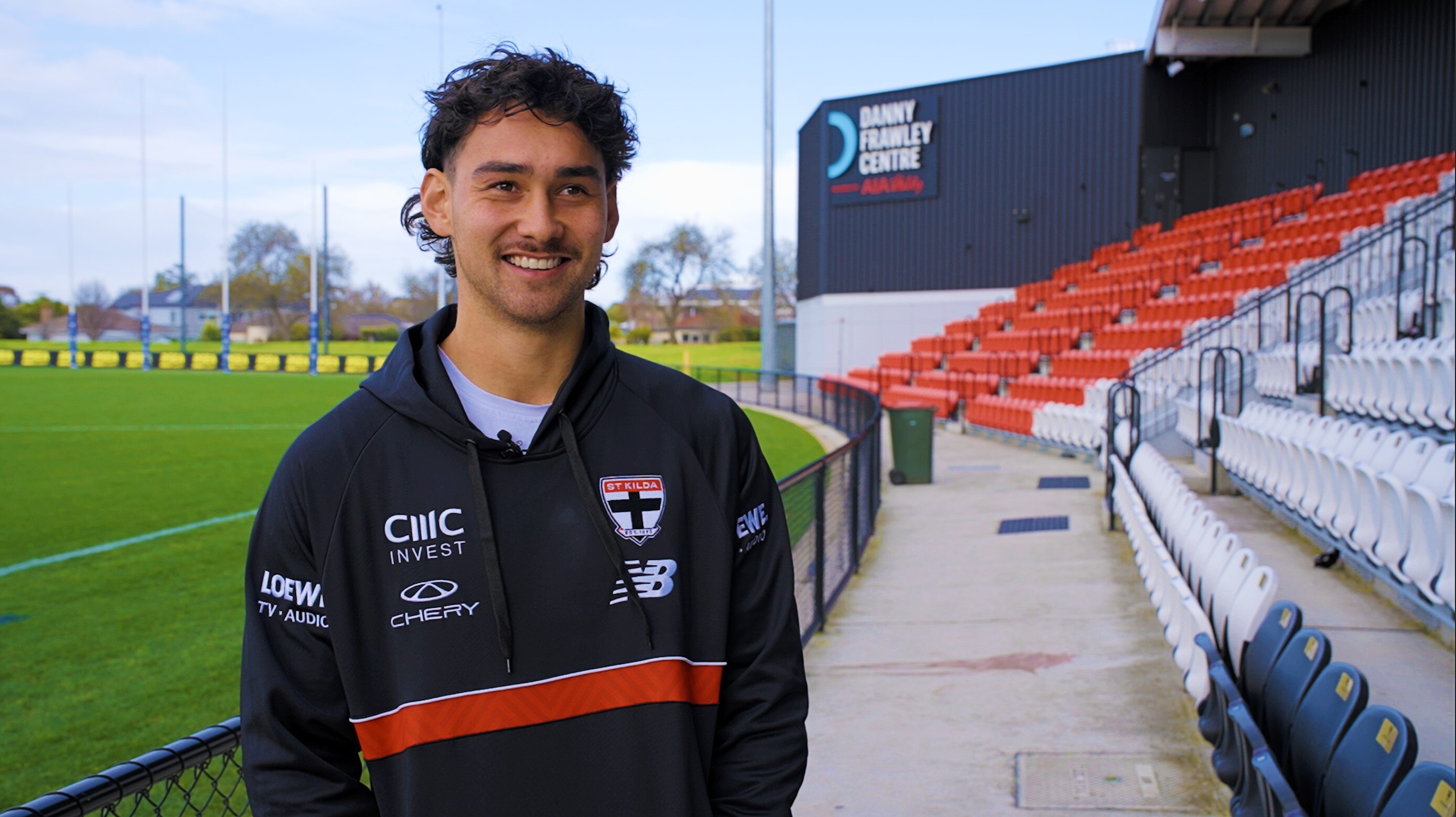 Man with wavy hair wearing sports top looks toward camera