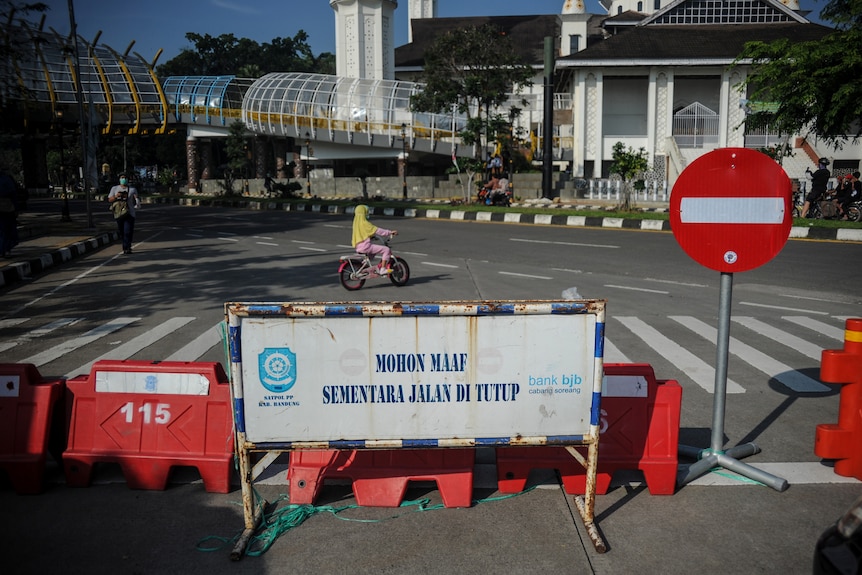 A girl on an Indonesia city street rides a bicycle behind a temporary road barrier.