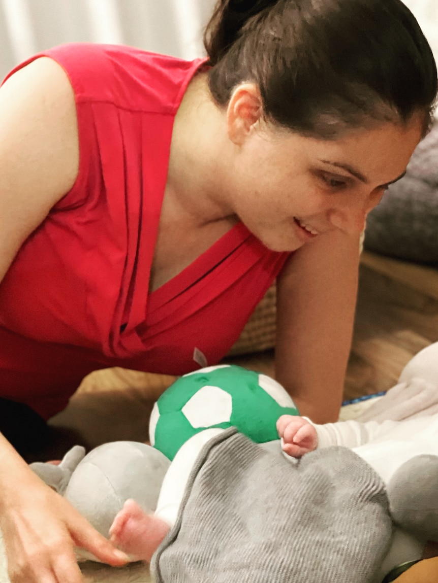 Nas Campanella leans over her baby son Lachie, who is lying on the floor surrounded by soft toys