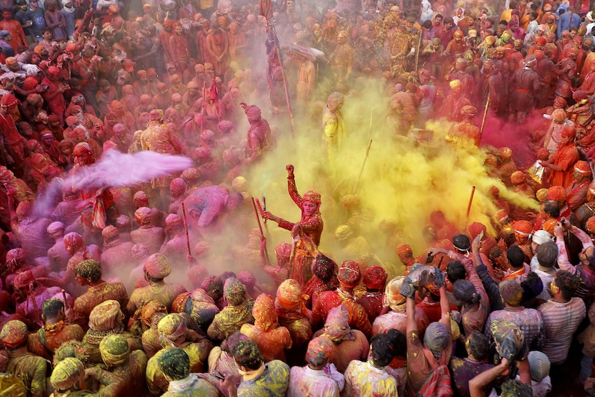 A huge group of tightly packed men throwing around brightly coloured powder