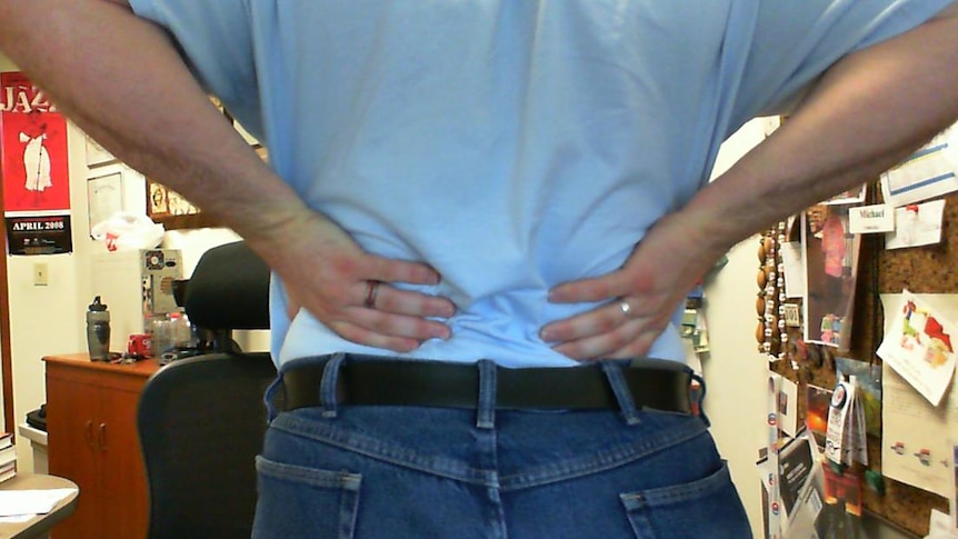 A photo of a person holding onto their back in response to back pain.