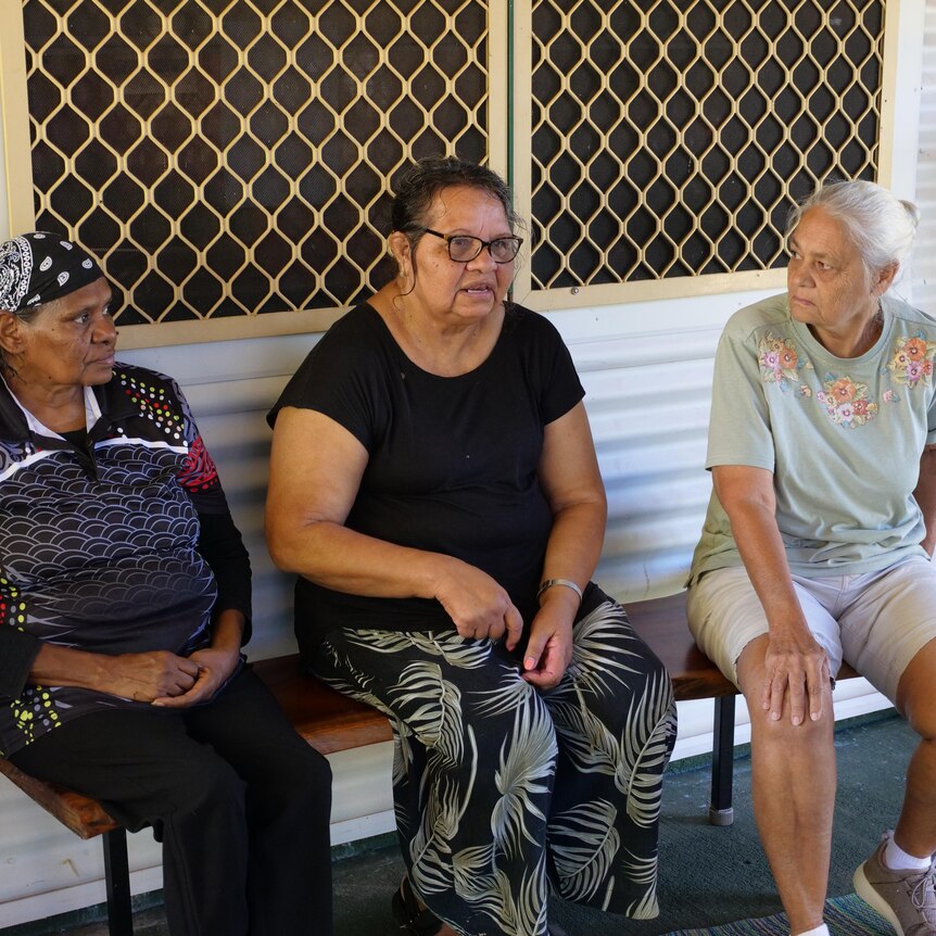three indigenous women sit on a bench talking