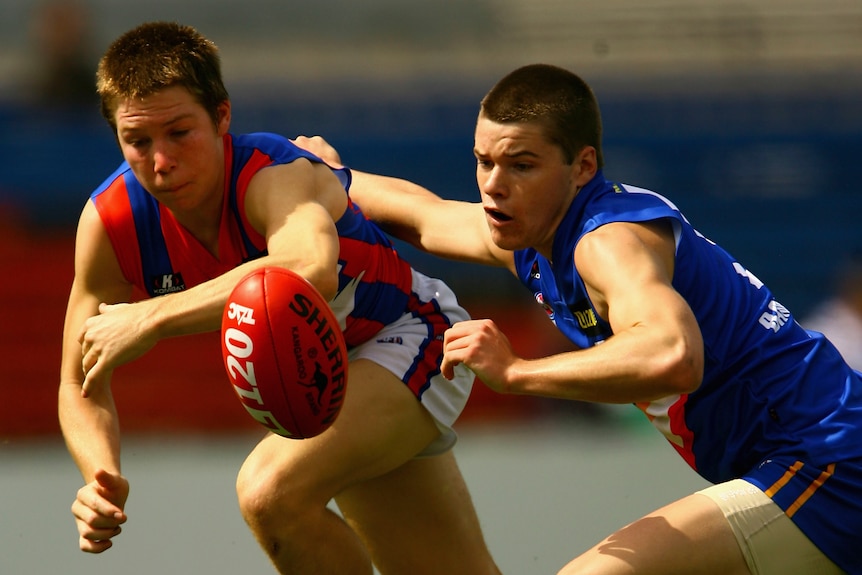 Two young Australian rules players go in with eyes on the ball while they try to get there first or stop the other player.