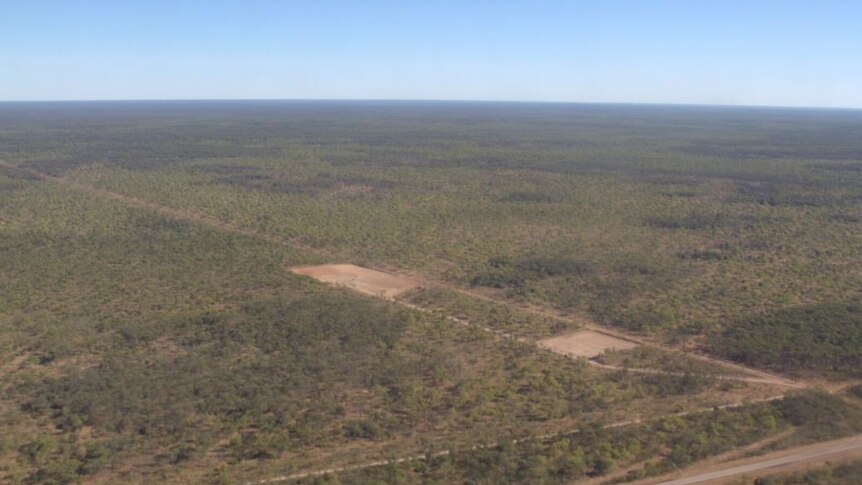 an aerial shot of a small cleared area in scrub with a road running through the bottom.