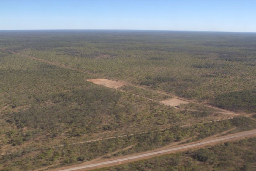 an aerial shot of a small cleared area in scrub with a road running through the bottom.