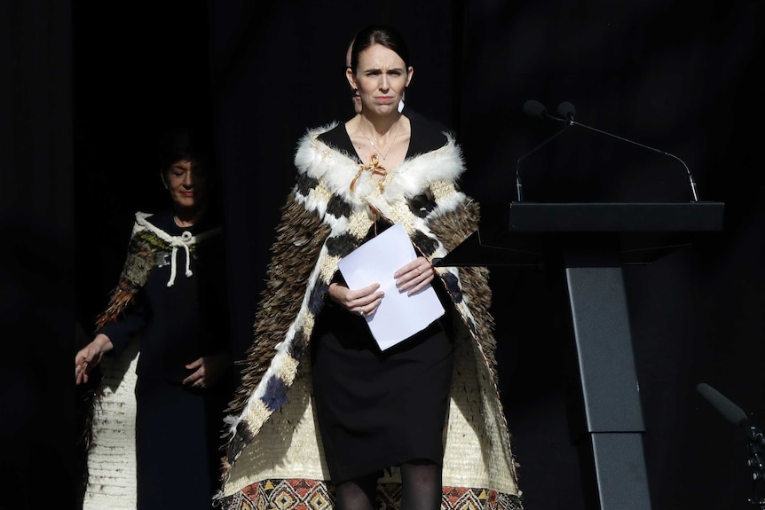 Jacinda Ardern wears a black dress and traditional cloak as she walks to towards a podium