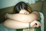 A girl hides her face behind her arms.