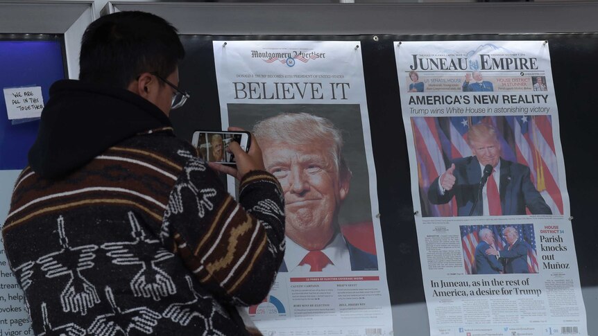 A Chinese man photographs the front pages of newspapers showing a Donald Trump election victory.