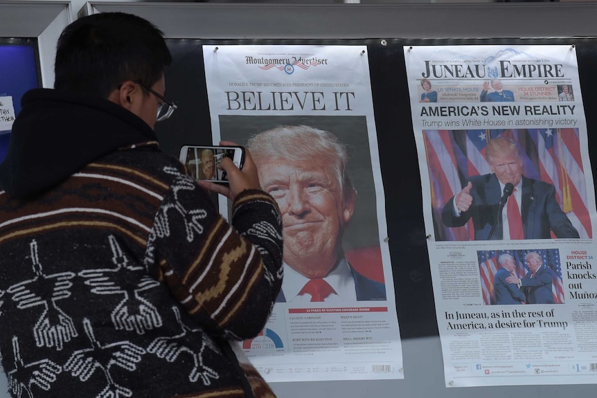 A Chinese man photographs the front pages of newspapers showing a Donald Trump election victory.