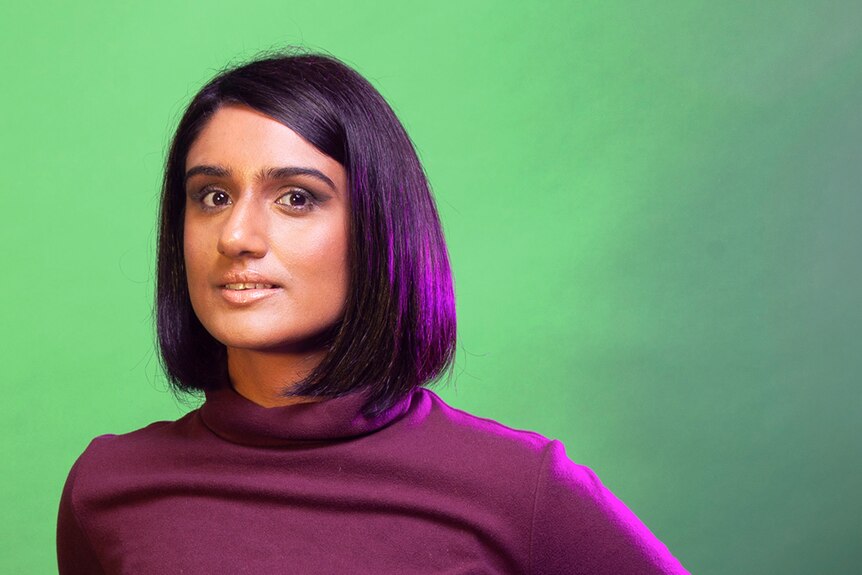 An Indian Tamil woman with a black bob looks into the camera. She is wearing a turtleneck, and has her hands on her hips. 