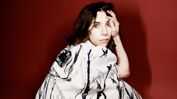 PJ Harvey crouches on the floor, hand on forehead, wearing white dress with black striped trees on it