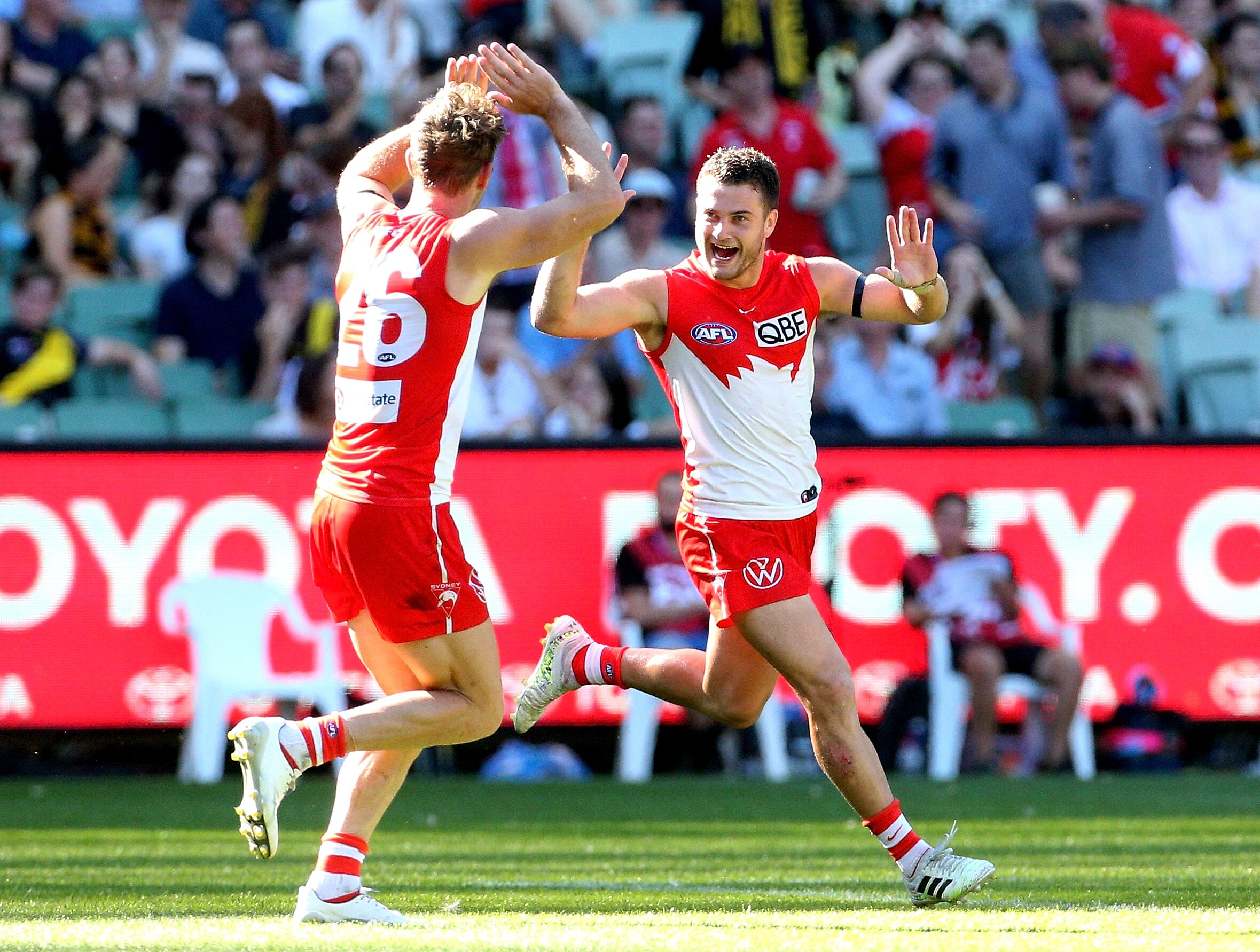 An AFL footballer grins and runs toward his teammate in celebration.