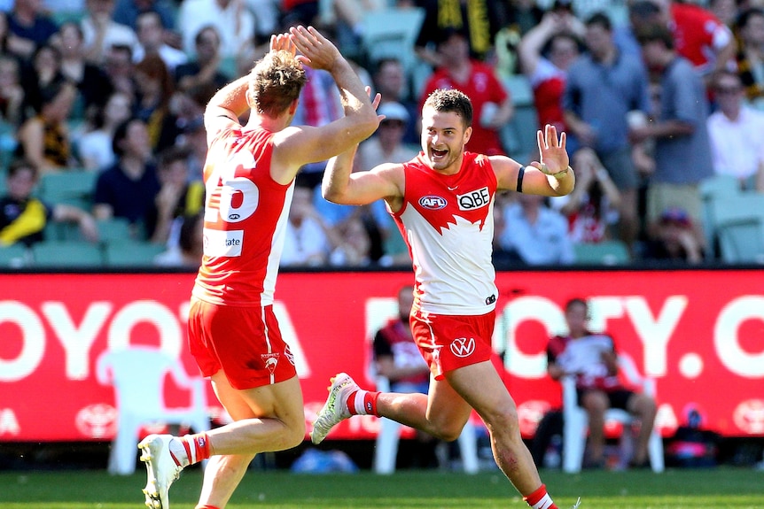 An AFL footballer grins and runs toward his teammate in celebration.