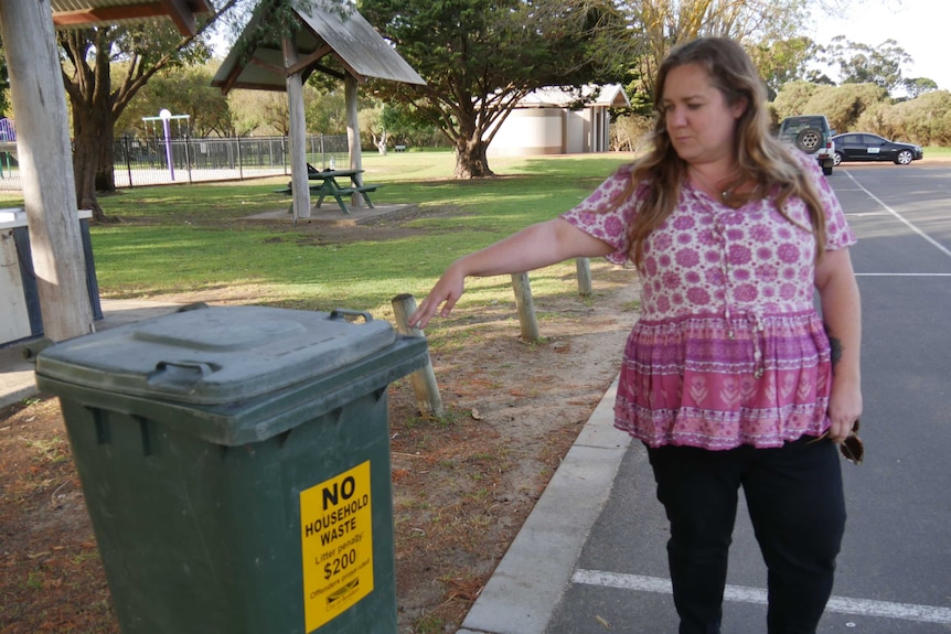 Wildlife carer Sasha Boundy wearing a pink and white dress standing in a car park next to a park pointing to bin.