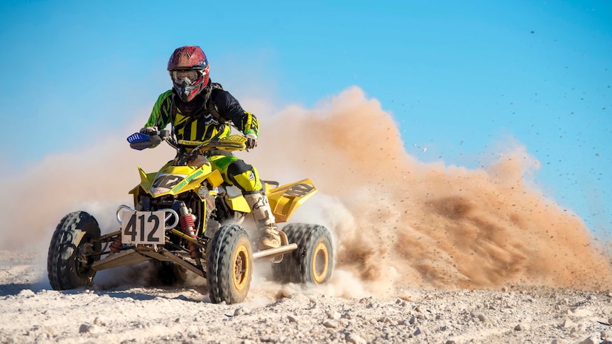 A quad bike leaves a train of dust as it revs along a direct racetrack.