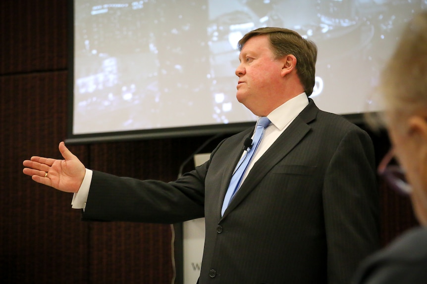Peter Daly stretches his arm out in the direction of an audience member during a speech at a business function.