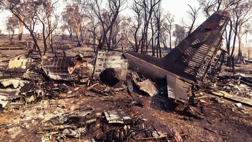 ground view of a destroyed and burnt out plane surrounded by burnt trees