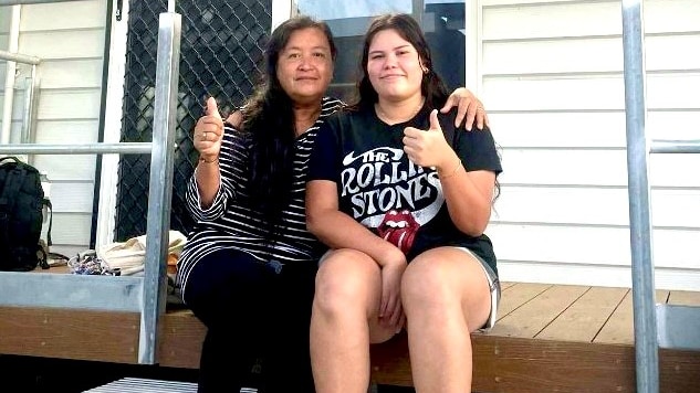 A woman and teenage girl give a thumbs up while sitting on the steps of a donga
