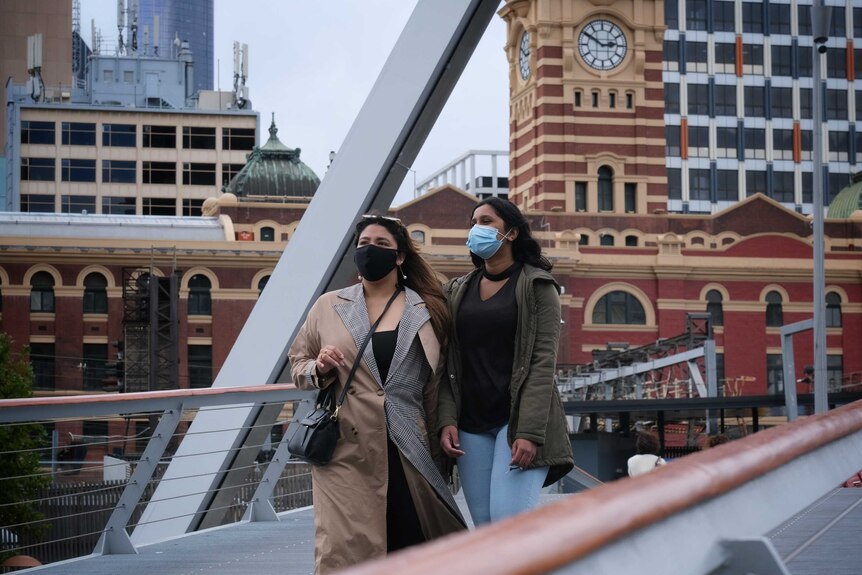Two women wearing face masks and earthy coloured coats in Melbourne.