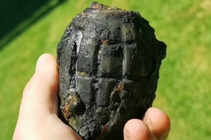 A hand olds a dark object with the distinctive criss cross of a grenade.