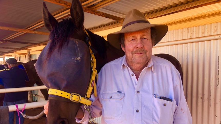 Terry Brennan standing next to his racehorse in holding pens at Meekatharra Race Track.