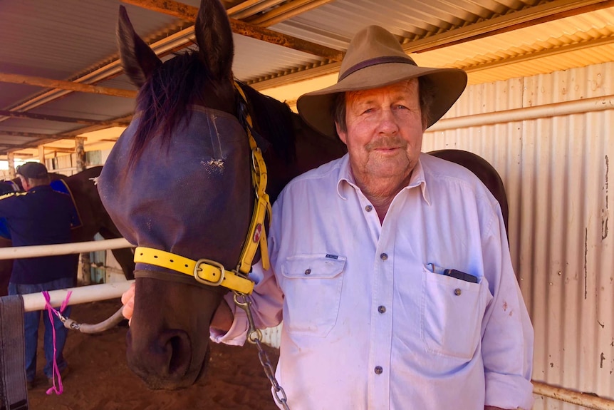 Terry Brennan standing next to his racehorse in holding pens at Meekatharra Race Track.