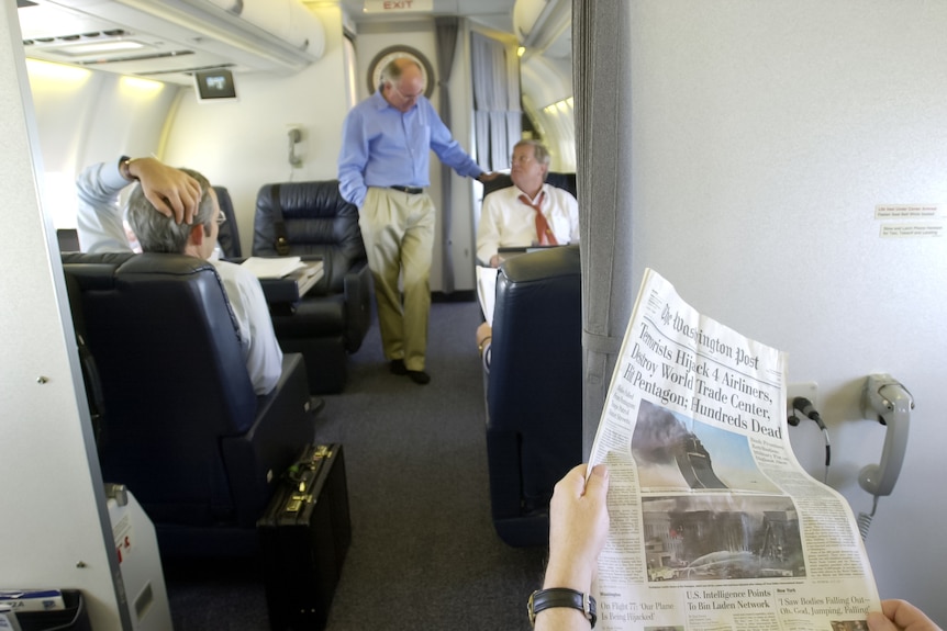 John Howard on a plane with a newspaper in the foreground with the twin towers on the front page