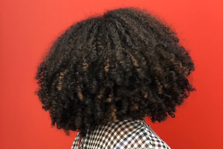 A woman with curly dark hair against a red background.