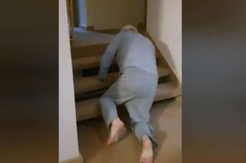Footage of an elderly man crawling on his hands and knees