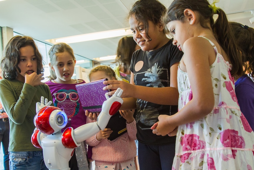 Young Indigenous girls use a iPad to write code to make a robot dance.