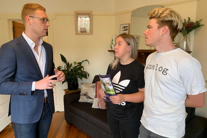 A young couple in a house listen to a man talking