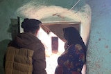 A pregnant women leans against a door frame as a man stands next to her.