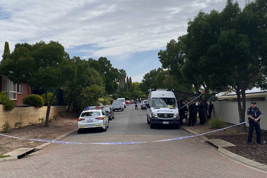 A street with police tape blocking it. A police officer, police car and a van are nearby.