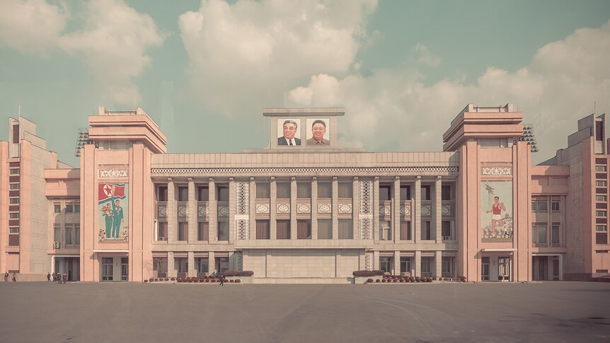 A grand Soviet-era stadium is seen from a distance with an empty square in front of it, decorated with North Korean frescoes.