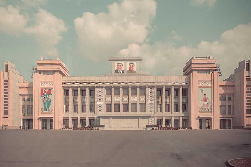 A grand Soviet-era stadium is seen from a distance with an empty square in front of it, decorated with North Korean frescoes.