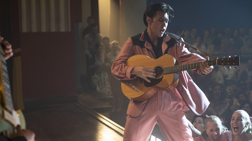 man in pink suit playing the guitar on stage