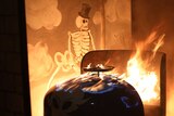 Re-enactment of carriage on fire with skeleton painting in background.