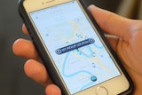 An Uber user holds a mobile phone displaying the app screen with the location set to Brisbane
