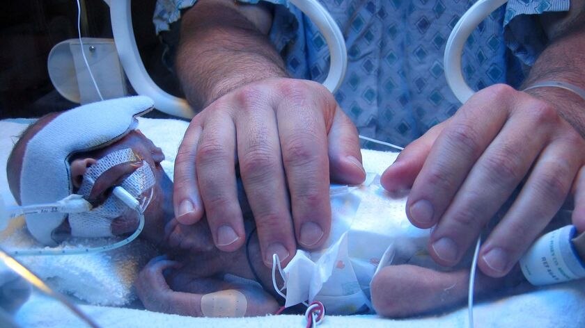 Jill' husband lays his hands on their premature baby boy.