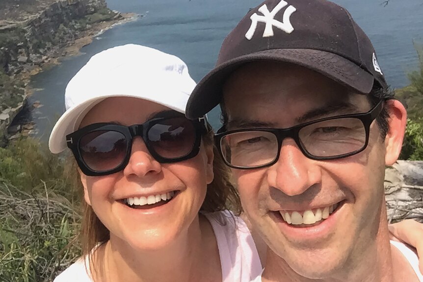 A man and a woman smiling as they take a selfie on top of a coastal headland