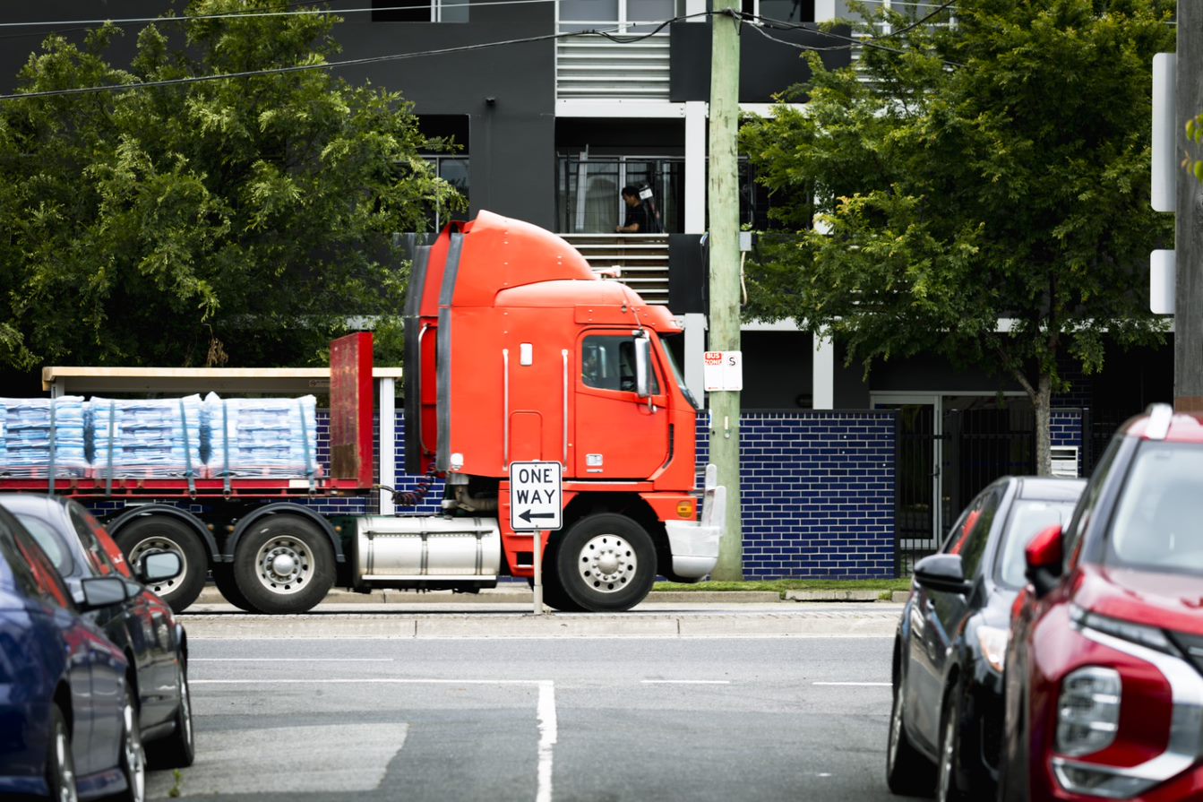 Um caminhão passa por uma rua residencial em frente a um prédio de apartamentos