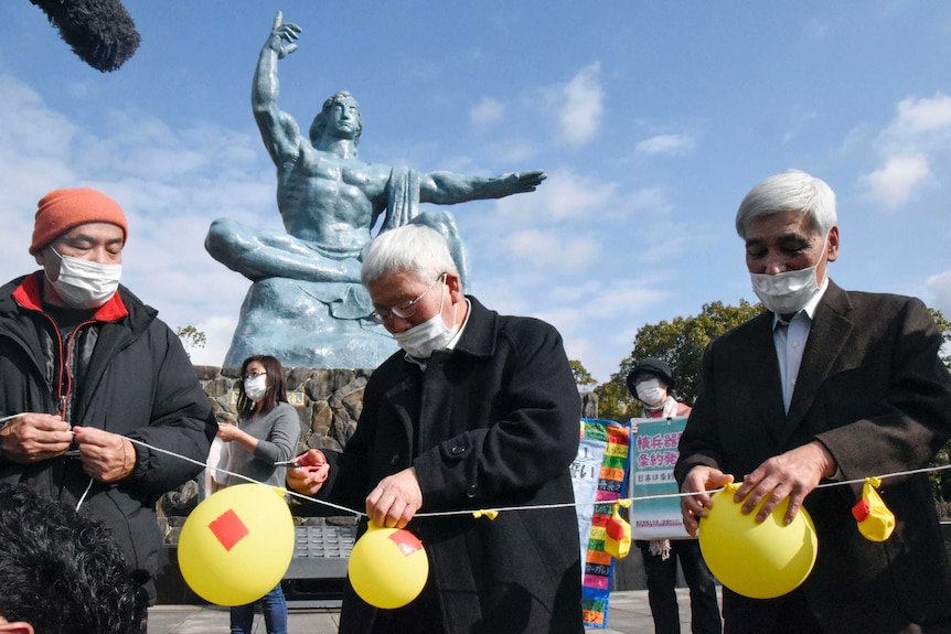 Men in masks deflate yellow balloons in a memorial park in Nagasaki