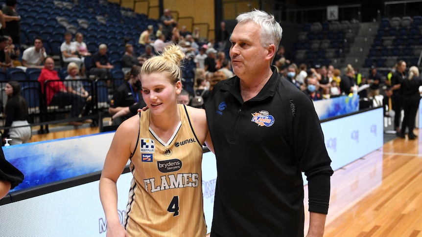 Basketballer Shyla Heal stands at the edge of a court as she and her father and coach Shane Heal have an arm around each other.