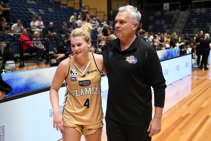 Basketballer Shyla Heal stands at the edge of a court as she and her father and coach Shane Heal have an arm around each other.