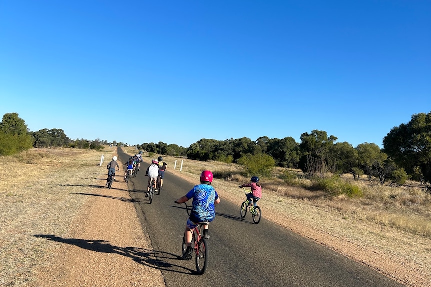 Children on bikes down straight road in outback