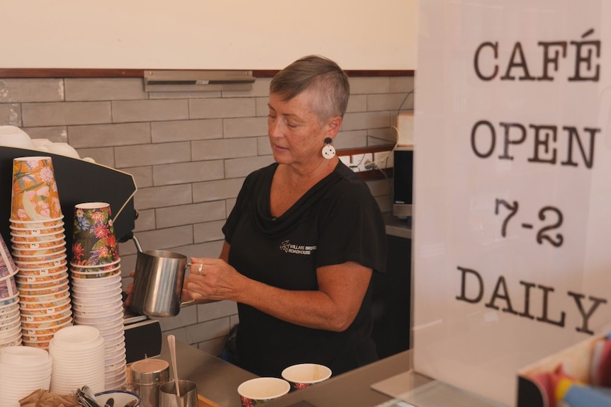 A woman makes a coffee behind a counter.