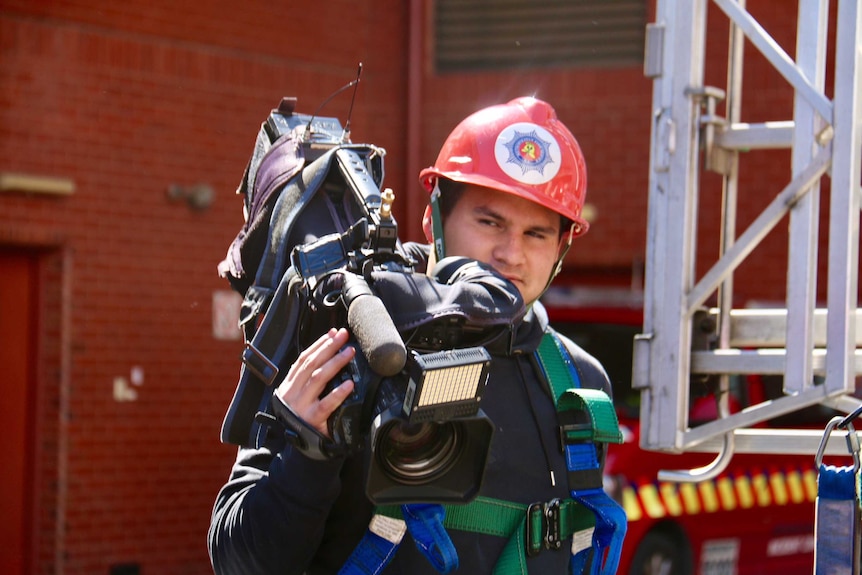 Haidarr Jones holding camera and wearing a red fireman's helmet.