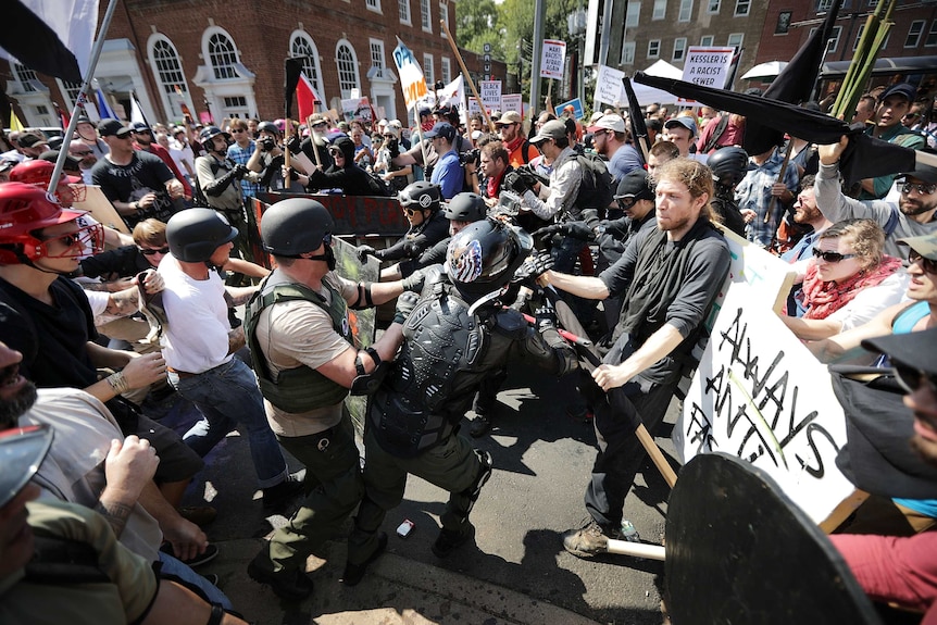 Two groups of protesters with signs from opposing sides moving towards each other the street, with some grabbing at each other.