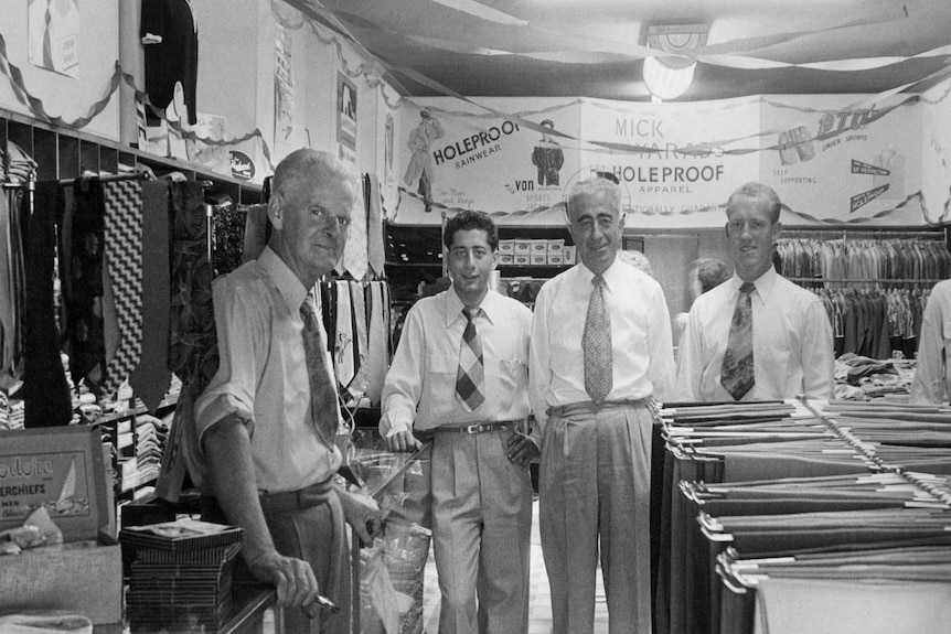 A black and white photo showing a group of men standing in a clothing store, possibly taken in the 1950s.