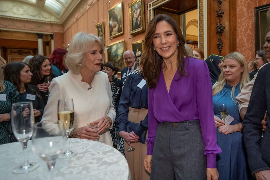 Queen Camilla and Princess Mary stand next to a table filled with champagne flutes